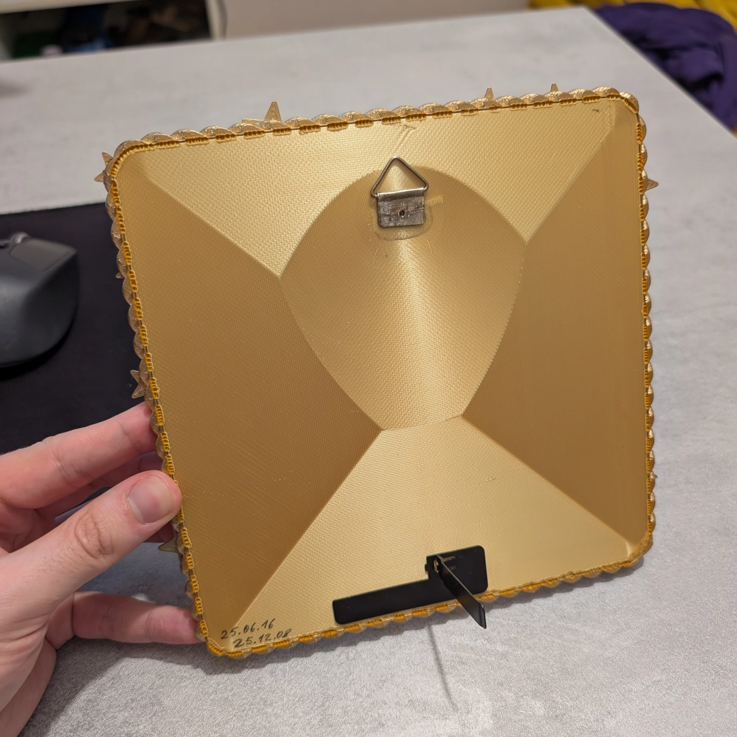 Užbaigto rėmelio nugarėlė su pakabinimo kabliuku ir kojele stovėjimui.