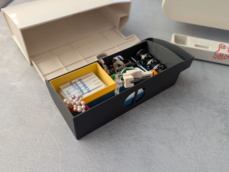 Siuvimo mašinos stalčiukas su dėžutėmis ir daiktais.