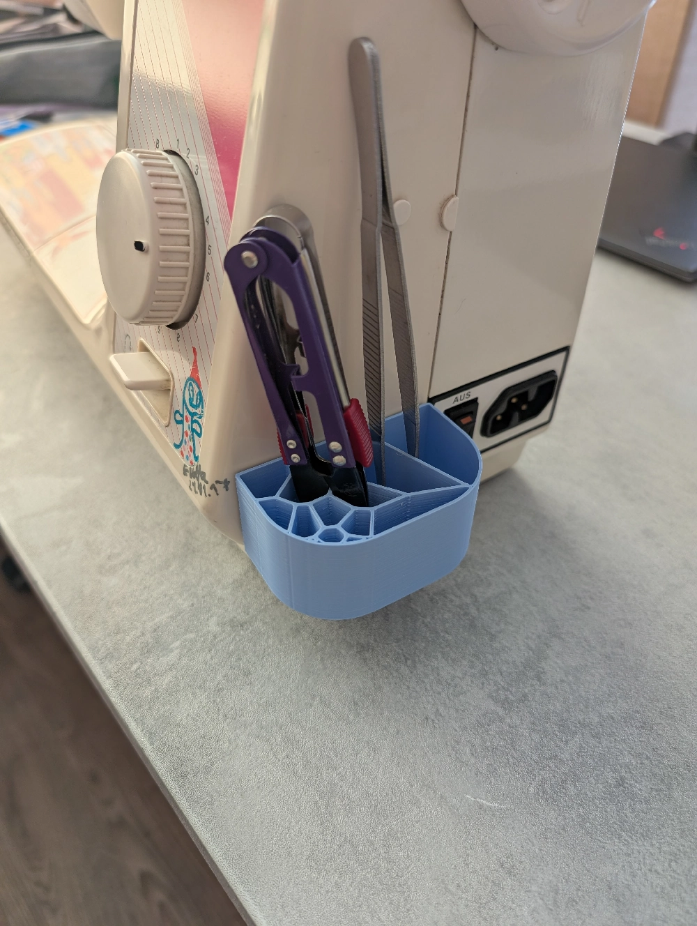 Reali Voronoi pieštukinė prie siuvimo mašinos šono su įrankiais.