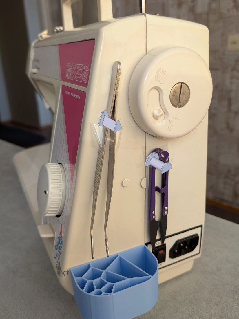 Siuvimo mašinos šonas su priklijuotais įrankiais ir nupieštais kabliukų 3D modeliais.