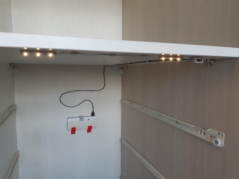 Stalčių komoda be stalčių su vidaus viršutinėje pusėje pritvirtintomis LED juostelėmis ir mygtuku bei powerbanku ant galinės sienelės.